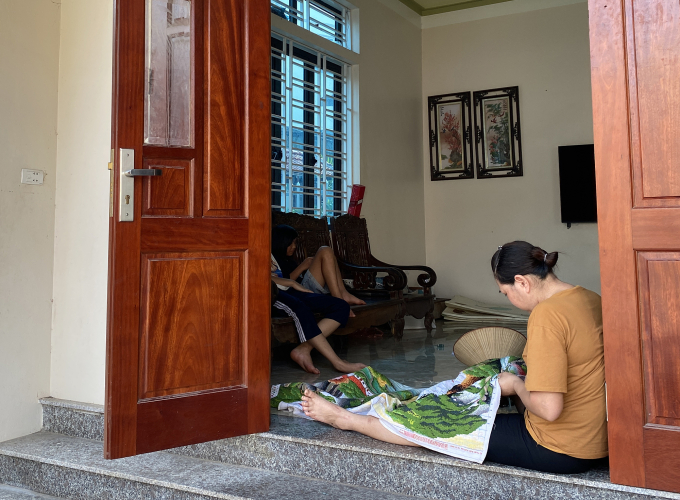 Một người phụ nữ tại xã Tiền Yên được công ty cho nghỉ làm cả ngày vì mất điện, đang phải lấy tranh ra thêu để quên cơn nóng, chiều 1/6. Ảnh: Quỳnh Nguyễn
