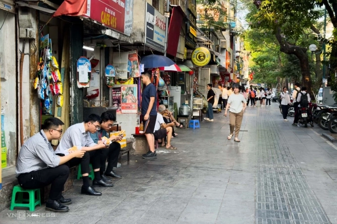 Người dân ngồi nép sát vào vỉa hè trên phố Lý Thường Kiệt, phường Hoàn Kiếm, Hà Nội, ăn bánh mì chiều 13/5. Ảnh: Quỳnh Nga